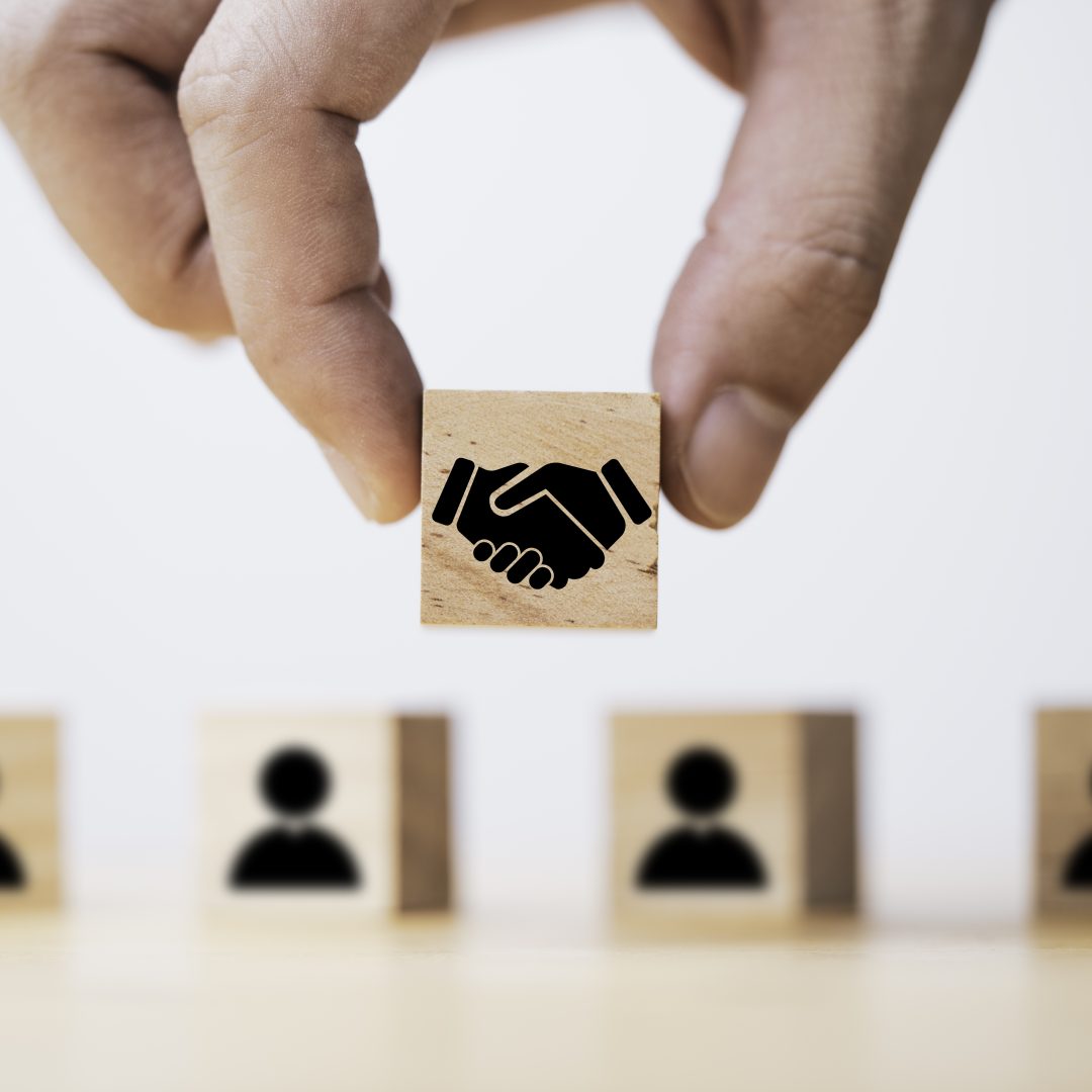 La photo représente une main tenant un cube en bois qui comporte un motif de poignée de main avec en arrière plan d'autres cubes avec des motifs de profil afin de symboliser l'action de devenir membre.